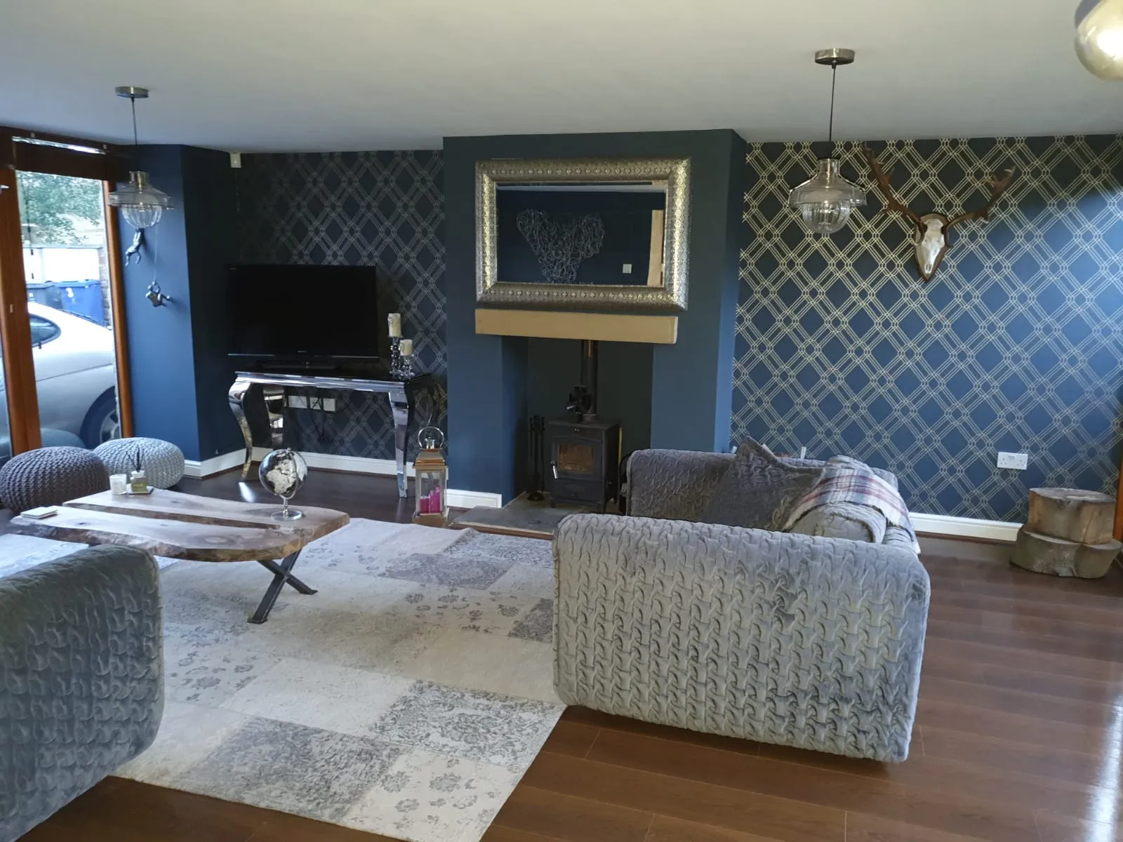Cosy Sheffield living room with deep navy patterned feature wall, framed mirror over a log burner, exposed wood floor and grey sofas. Painter and decorator work by Local Painter and Decorators Sheffield Hillsborough.